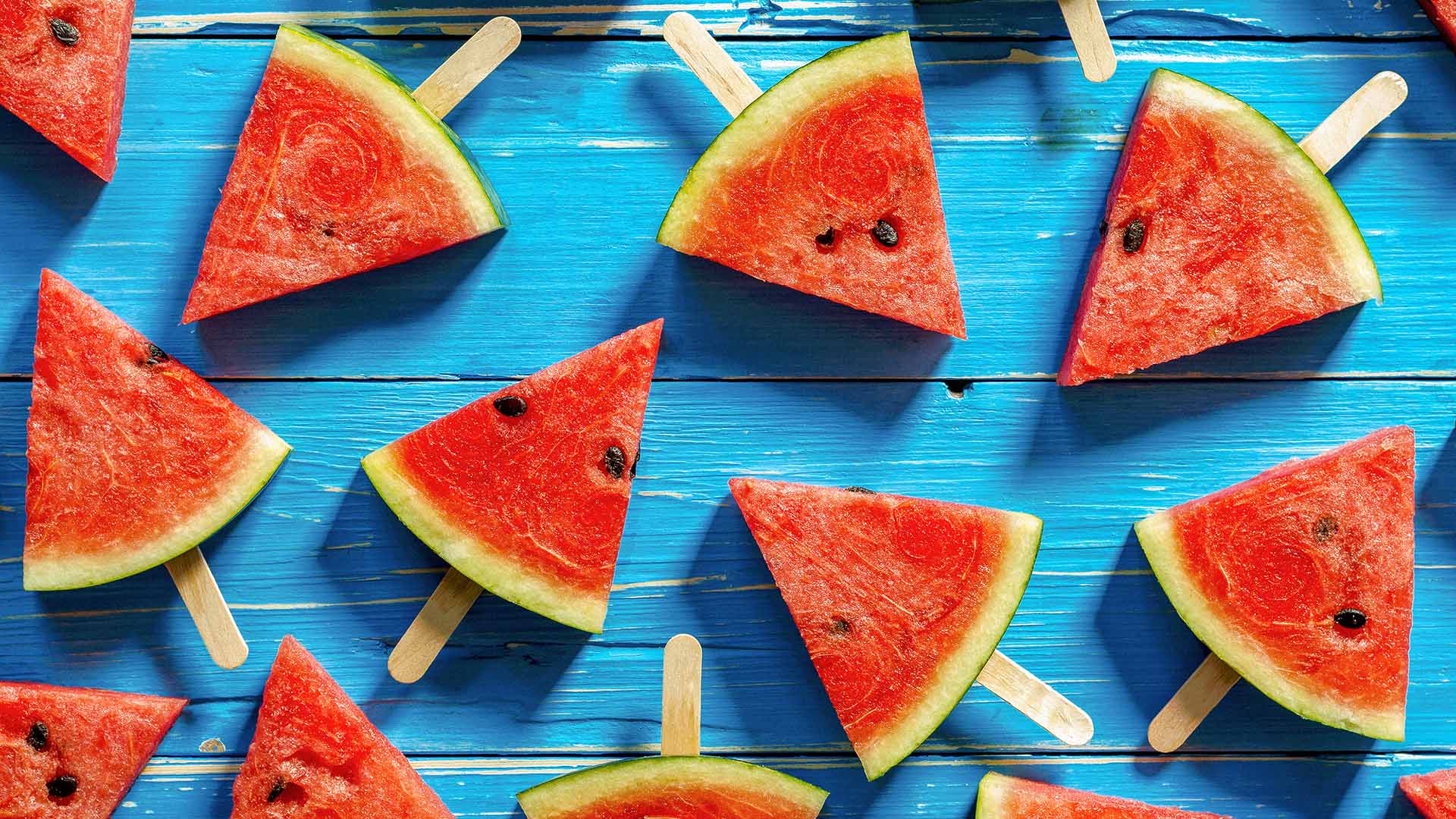 several watermelon slices with popsicle sticks arranged on a blue wooden surface