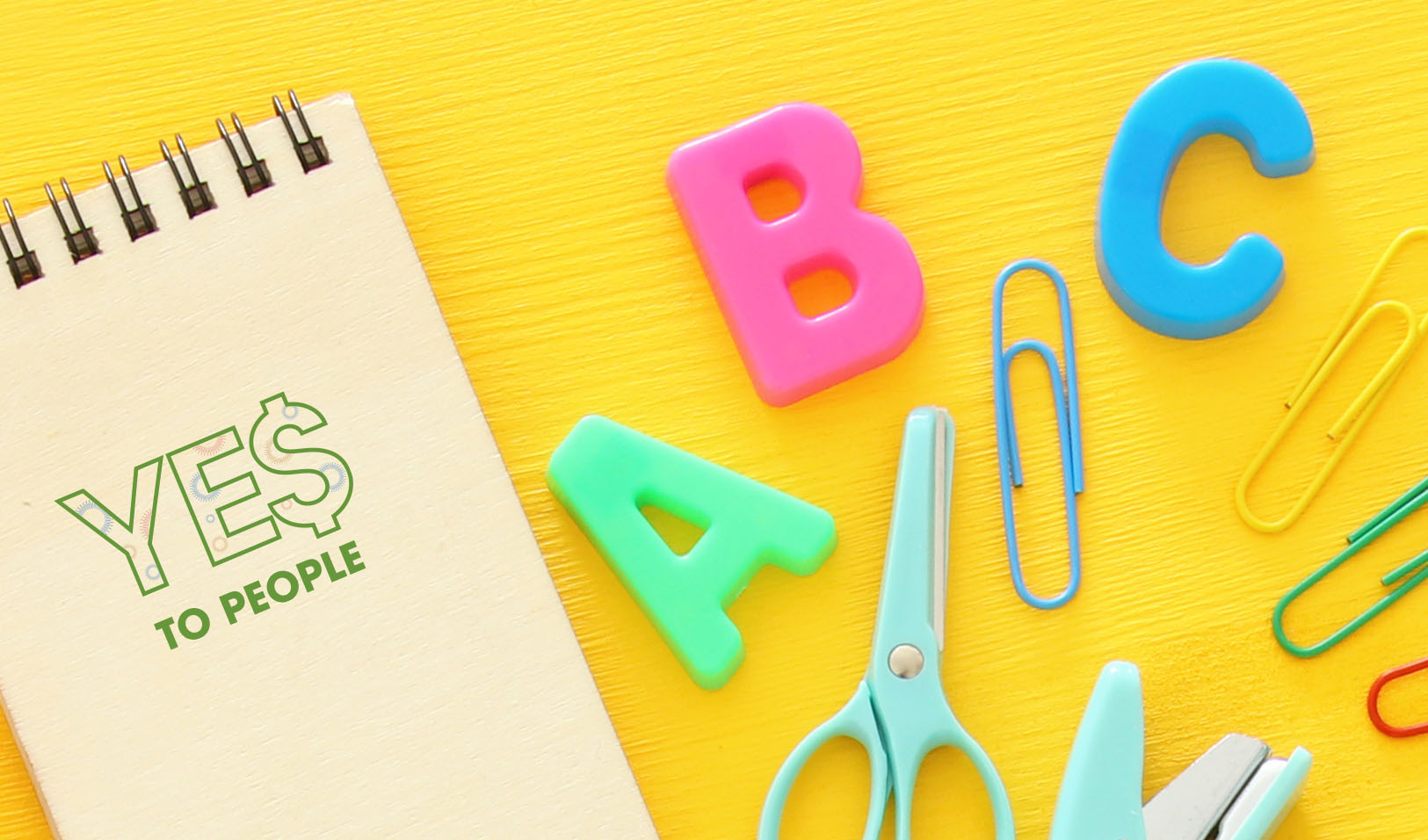 colorful school supplies including a notepad that says "YES To People" on it, all laying on a bright yellow background